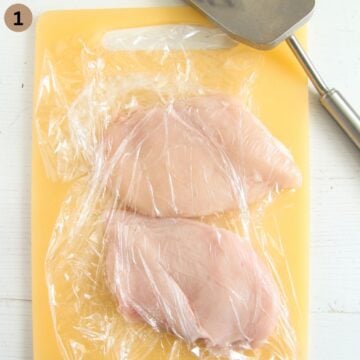 two pounded chicken breasts covered with plastic wrap and a meat mallet beside them.