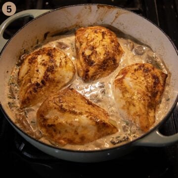 four chicken breasts simmering in creamy sauce in a pot.