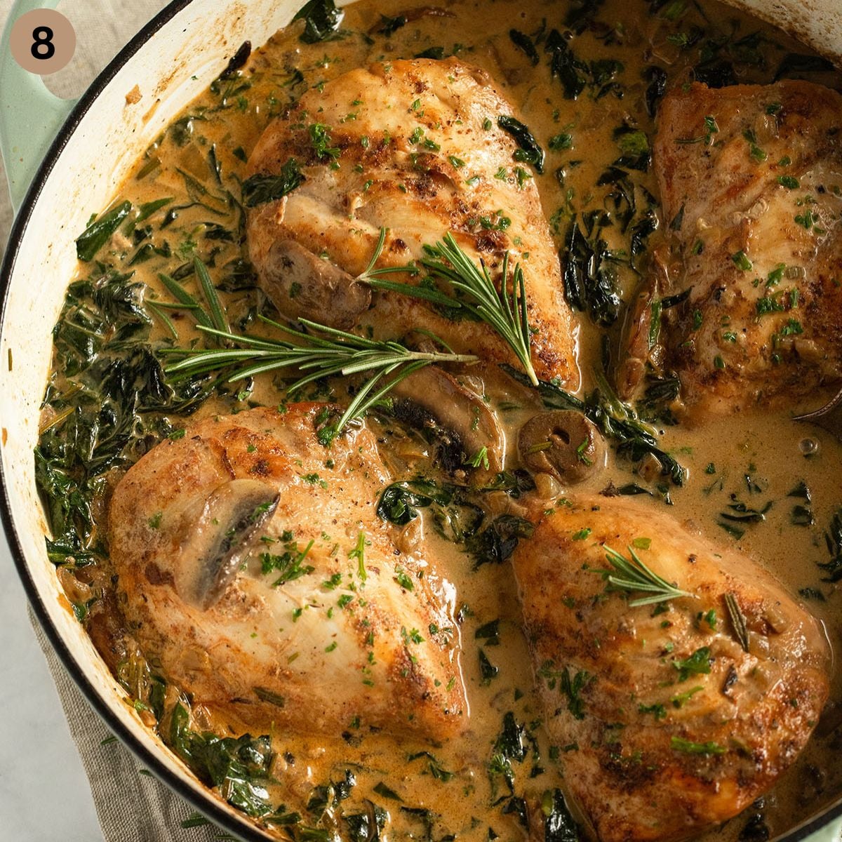 chicken breasts simmering in cream sauce with mushrooms and spinach.