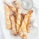 puff pastry twist sprinkled with confectioner's sugar and a small sieve near them.