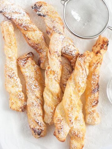 puff pastry twist sprinkled with confectioner's sugar and a small sieve near them.