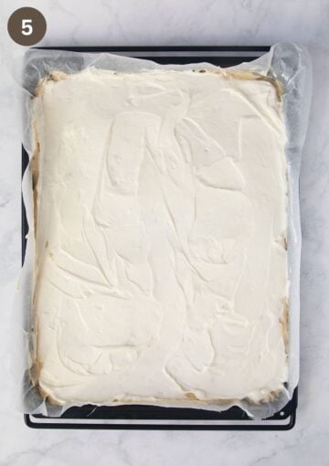 cream cheese filling spread on cake batter on a baking sheet.