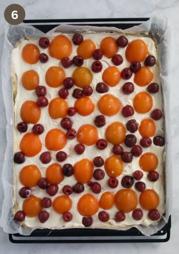 arranged apricots and cherries on cake batter on a baking sheet.