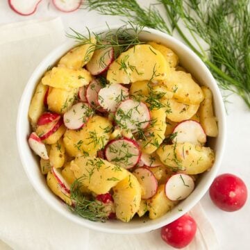 potato radish salad with dill in a bowl, more radishes and dill around it.