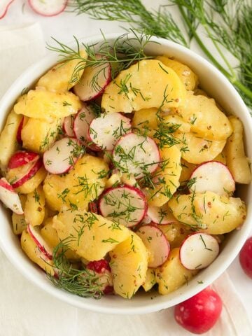 potato radish salad with dill in a bowl, more radishes and dill around it.
