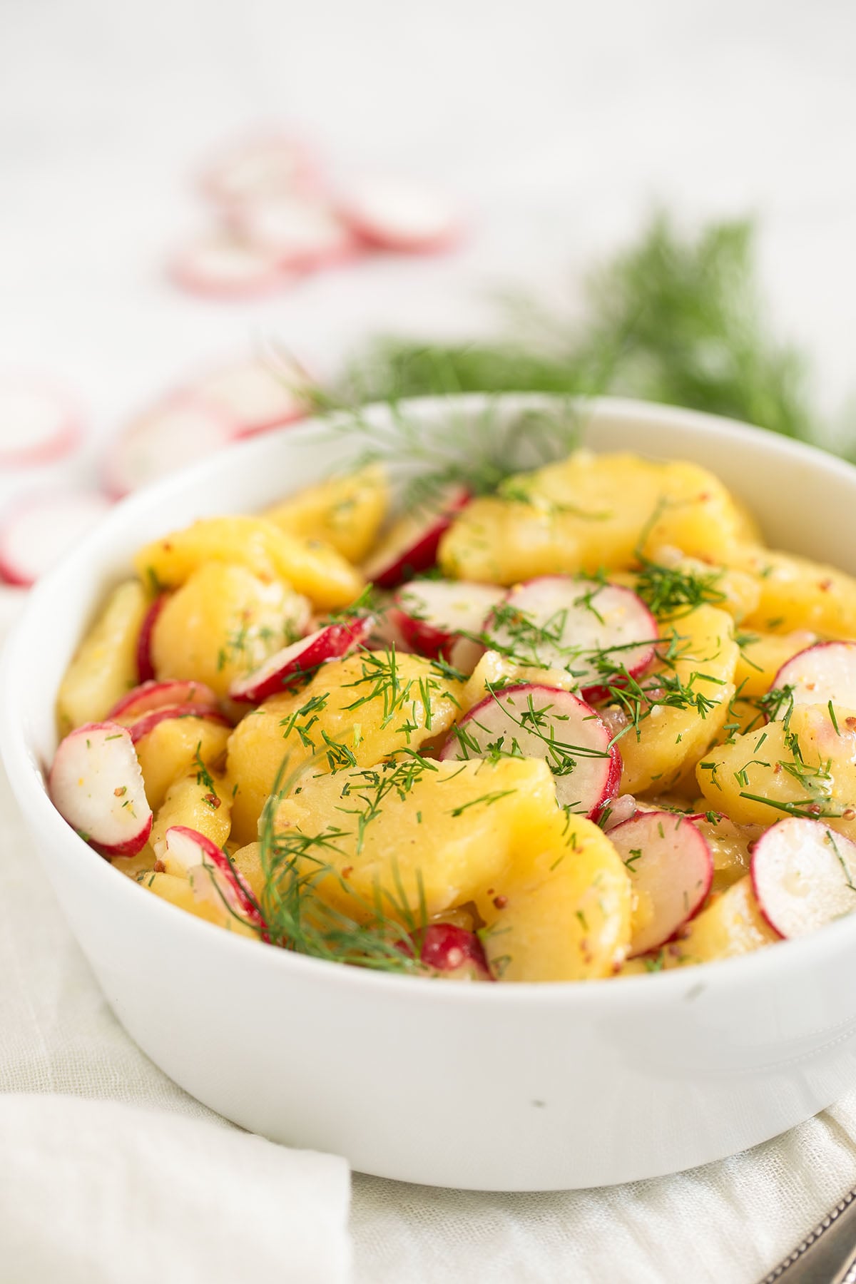 potato salad with radishes in a bowl and a bunch of dill behind it.