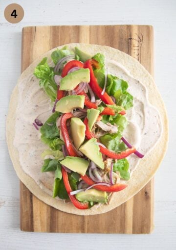 adding cubed avocado to tortilla wraps with vegetables and chicken.