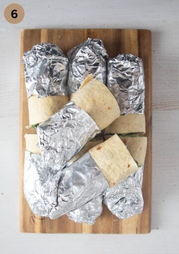 chicken wraps with the ends wrapped in foil on a cutting board.