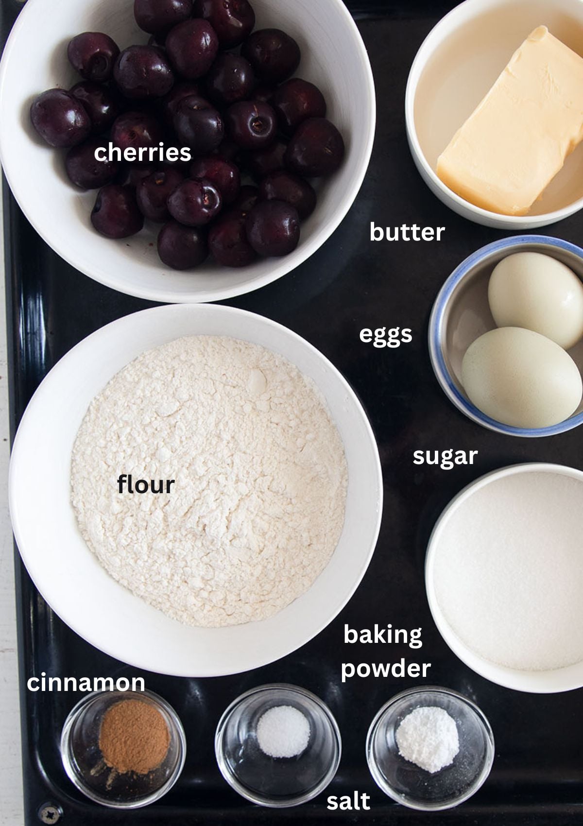labeled ingredients for making muffins with fresh cherries, sugar, flour, butter, and eggs.