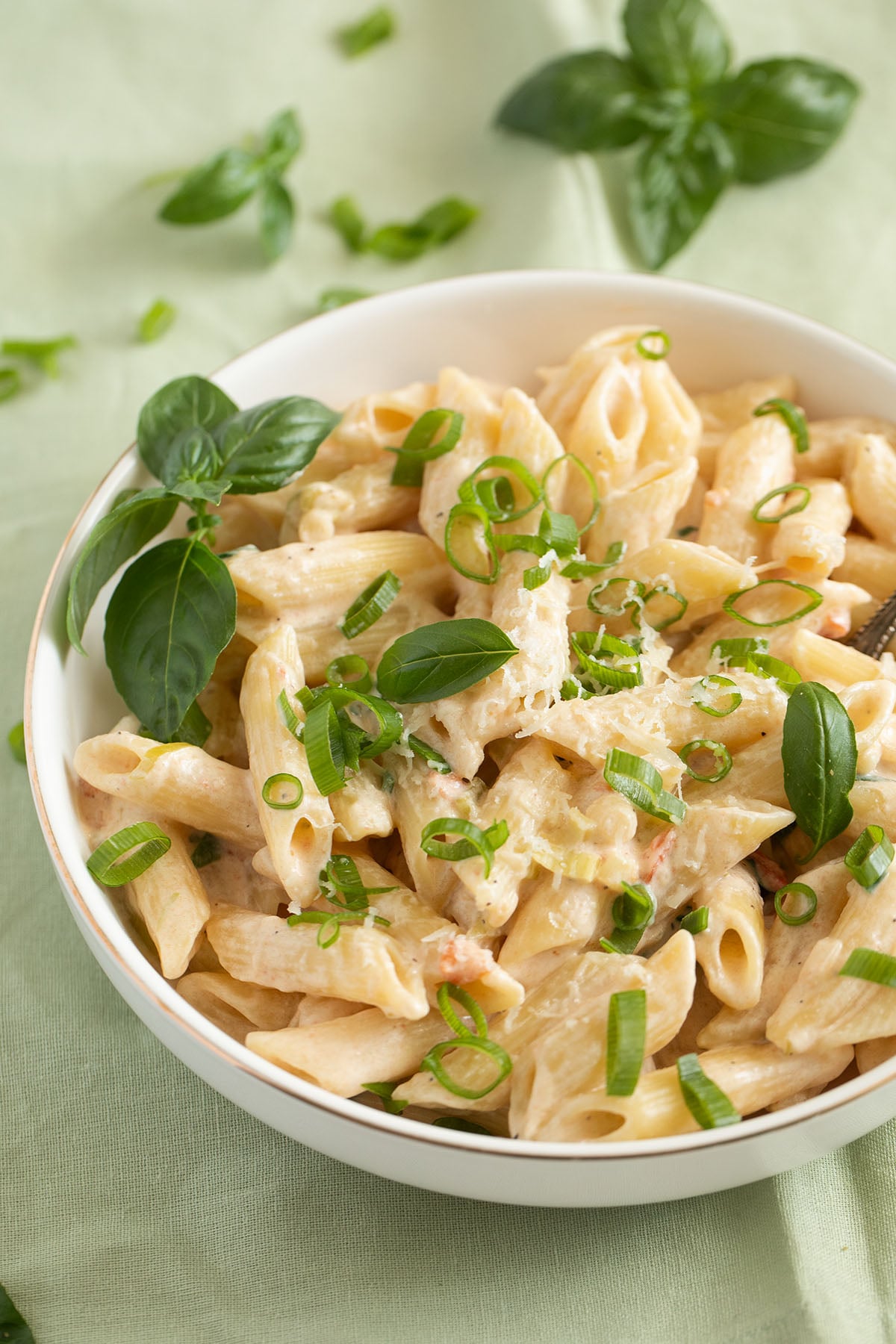 a bowl of green onion or scallion pasta in a bowl, some basil leaves in the back.