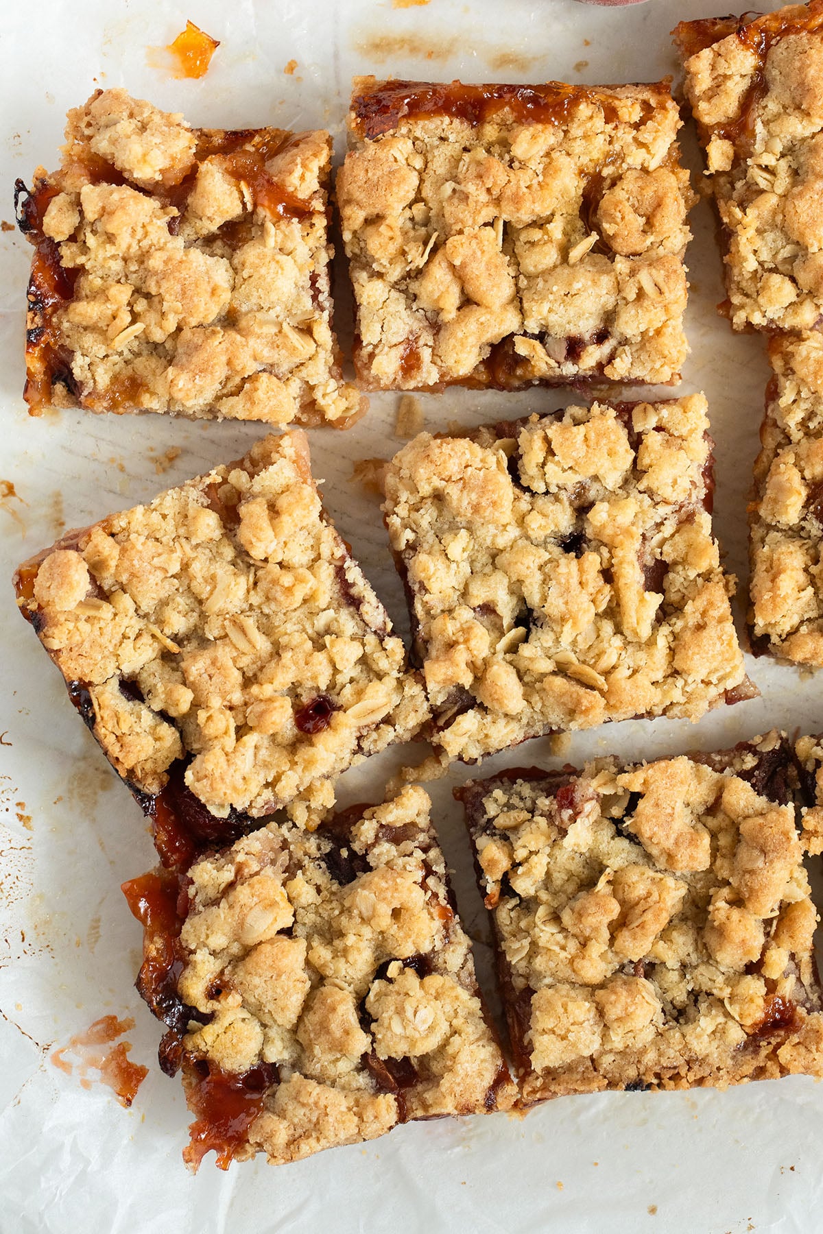 crumble bars filled with peaches and jam cut into squares on parchment paper.