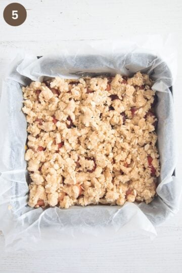 unbaked peach crumble bars in a baking dish line with white parchment paper.