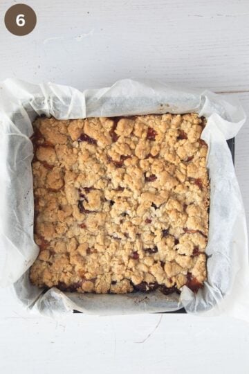 golden baked peach bars with crumbles in a baking dish lined with parchment paper.