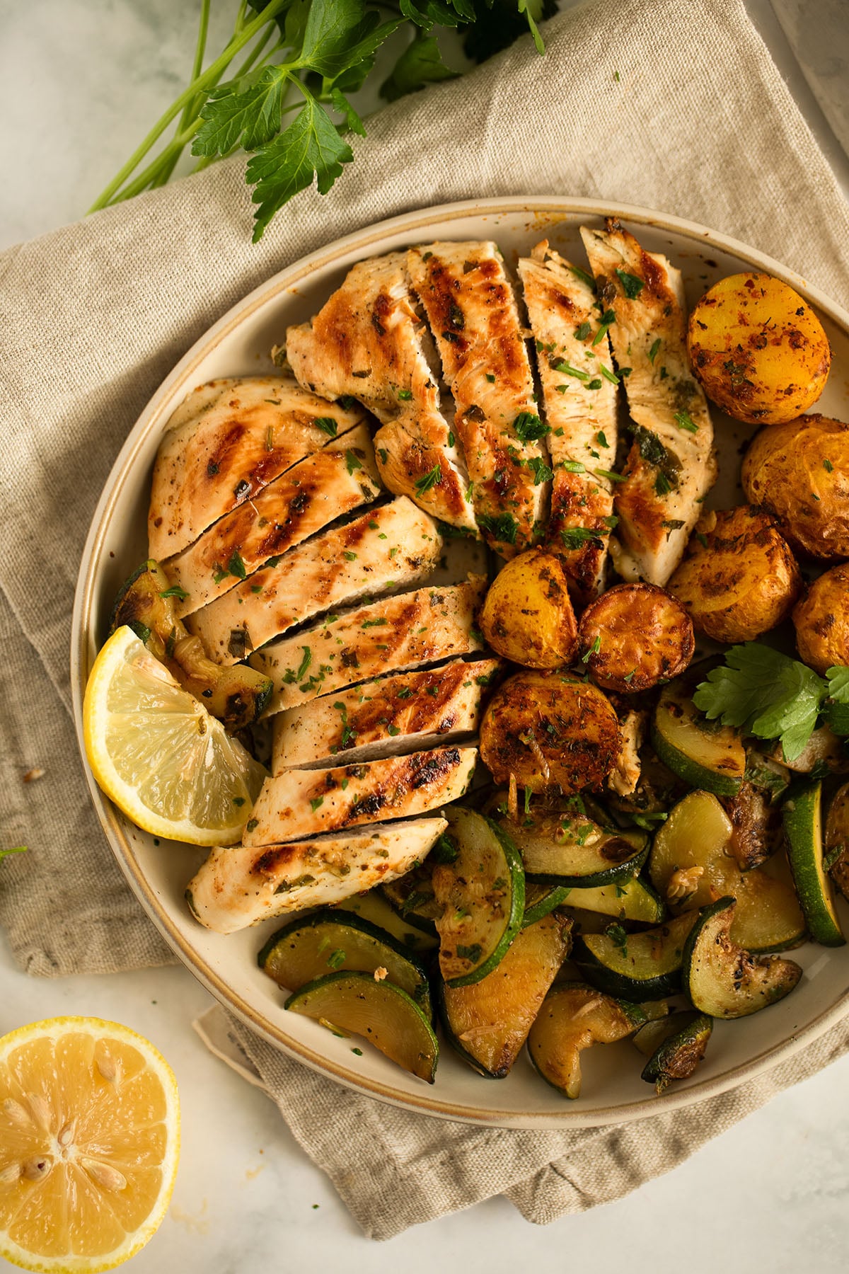 sliced chicken breasts served with sauteed zucchini and oven potatoes on a plate.