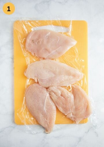 four pieces of raw chicken breast on a cutting board.