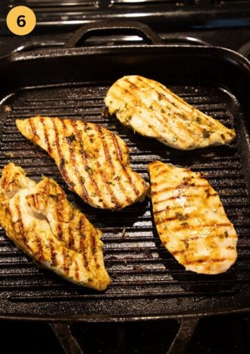 four pieces of chicken breast cooking in a grill pan showing the grill marks.