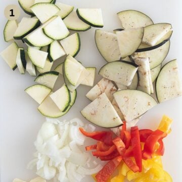 sliced eggplants, zucchini, peppers, and onions on a cutting board.