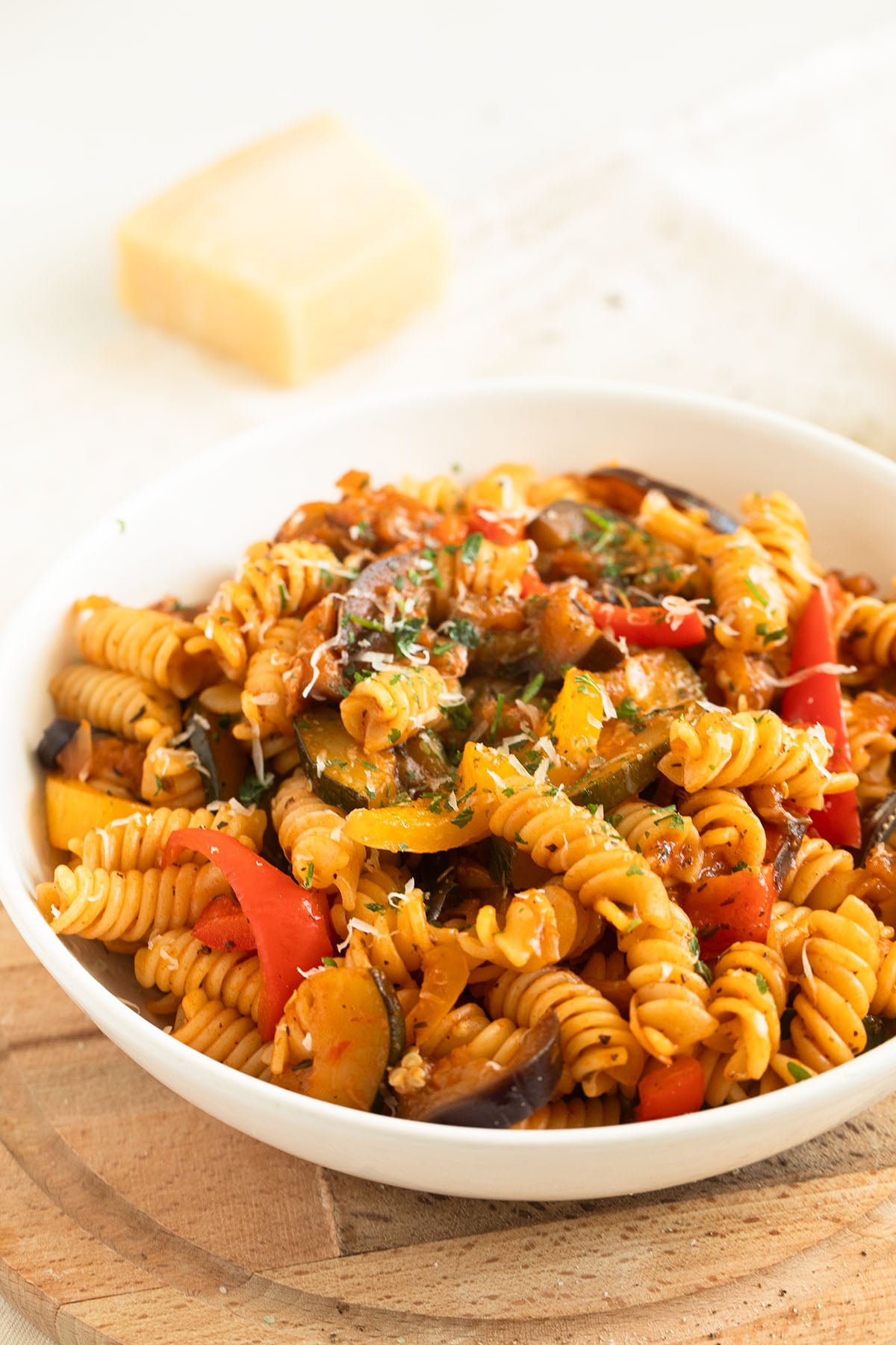 a bowl with ratatouille pasta and a wedge of parmesan behind it.