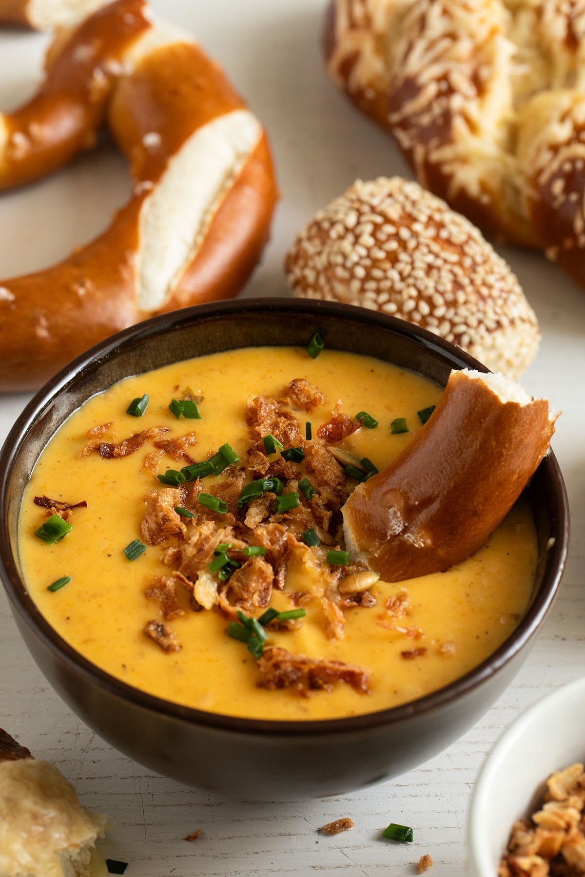 a piece of pretzel dipped into a bowl of warm, creamy beer cheese dip.