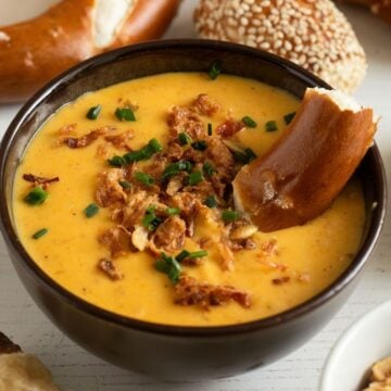 a bowl with creamy beer cheese pretzel dip topped with crispy onions and a pretzel piece inside.