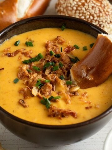 a bowl with creamy beer cheese pretzel dip topped with crispy onions and a pretzel piece inside.