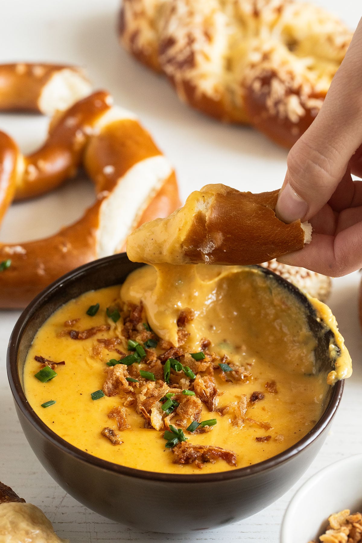 a hand lifting a piece of pretzel covered in warm, creamy beer cheese dip.