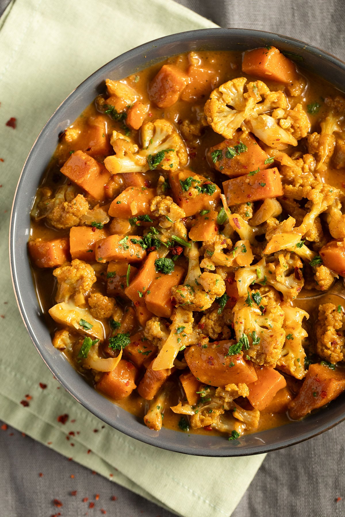 a bowl full of cauliflower and sweet potato curry sprinkled with herbs.