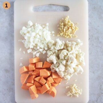 chopped cauliflower, sweet potatoes, ginger, garlic, and onion for making curry on a cutting board.