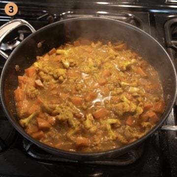 simmering sweet potato and caulliflower curry with coconut milk in a pan.