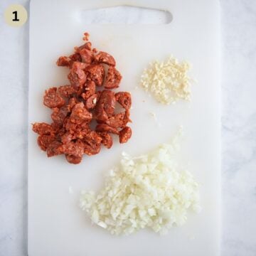chopped chorizo, onion and garlic on a cutting board for making chorizo pasta.