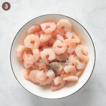 tossing shrimp with salt and pepper in a bowl.