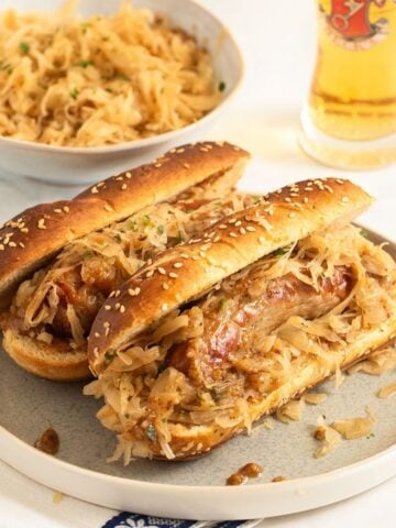 two bratwurst sandwiches, a bowl of sauerkraut and a glass of beer.