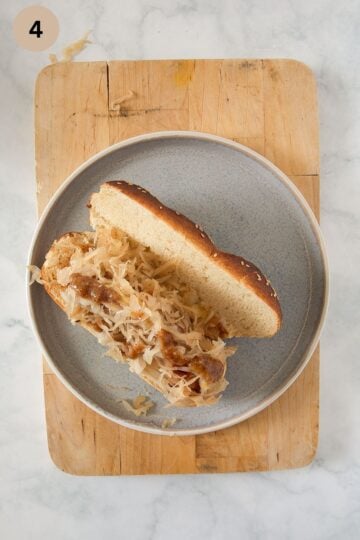 assembling a bratwurst sandwich in a pretzel bun with sauerkraut.