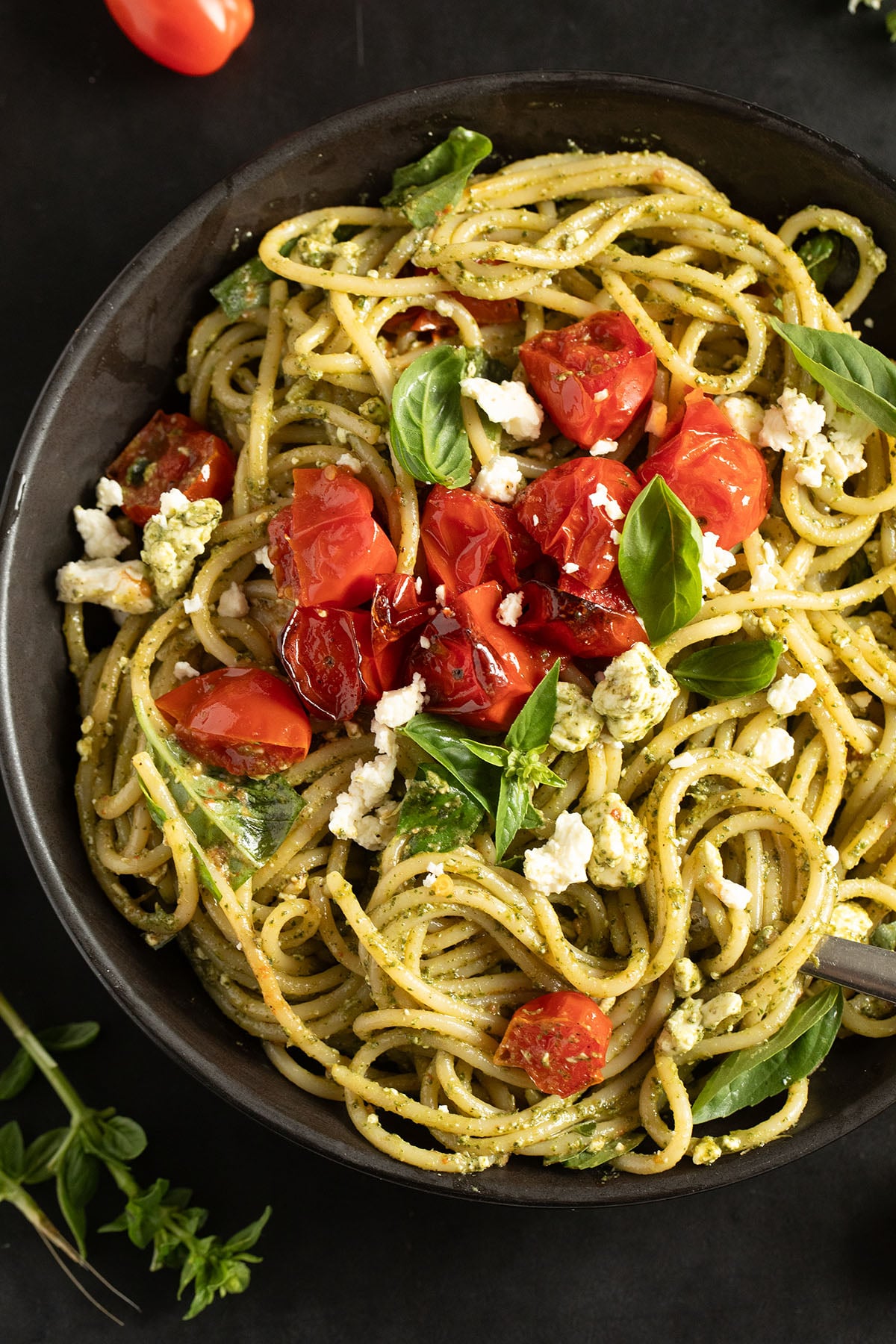 pasta with pesto, basil and feta topped with roasted tomatoes tomatoes and basil in a large bowl.