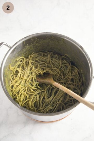 mixing cooked spaghetti with pesto in a pot using a wooden spoon.