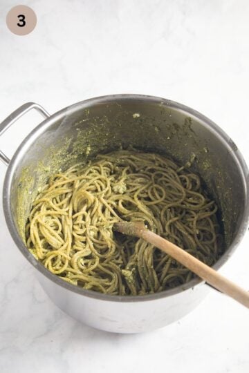 mixing pesto spaghetti with feta in a large pot with a wooden spoon.