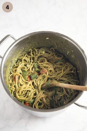 mixing pesto spaghetti with roasted tomatoes in a large pot.