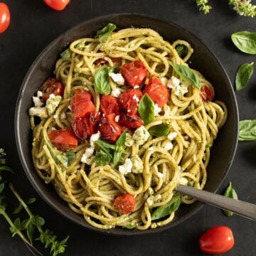 tangled feta pesto pasta topped with roasted tomatoes and basil in a bowl.