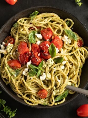 tangled feta pesto pasta topped with roasted tomatoes and basil in a bowl.