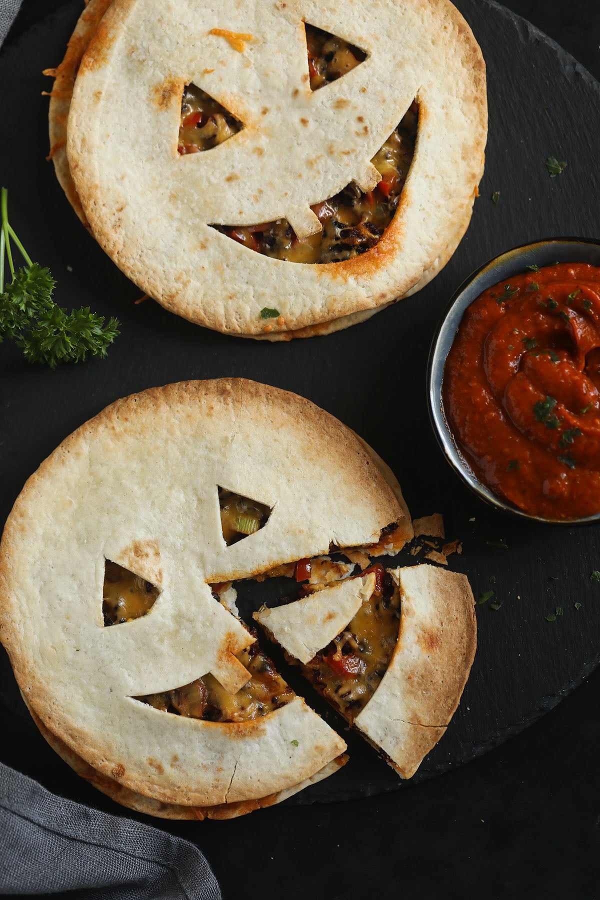 two jack'o'lantern-faced quesadillas, one with a cut triangle, and one small bowl of salsa.