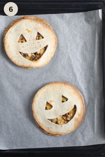 two jack'o'lantern faced quesadillas on a baking sheet.