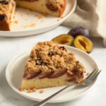 slice of plum crumble cake on a small plate with a fork.