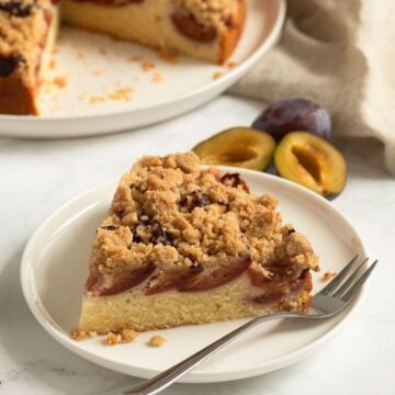 slice of plum crumble cake on a small plate with a fork.