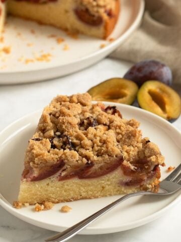 slice of plum crumble cake on a small plate with a fork.