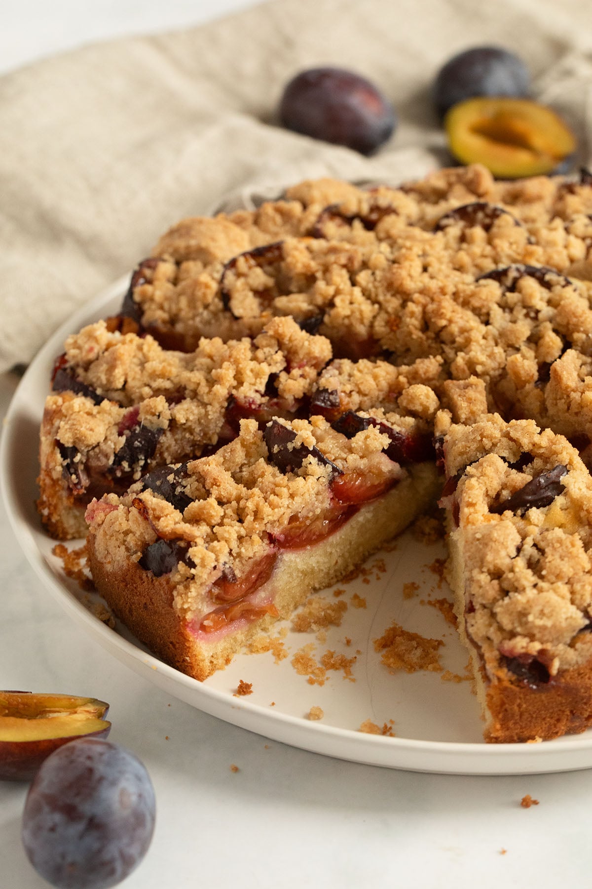 plum cake with crumbles cut into slices on a round platter.